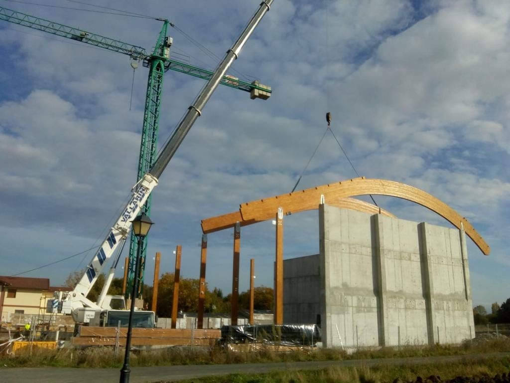 Una grúa está levantando una viga de madera frente a un edificio en construcción.