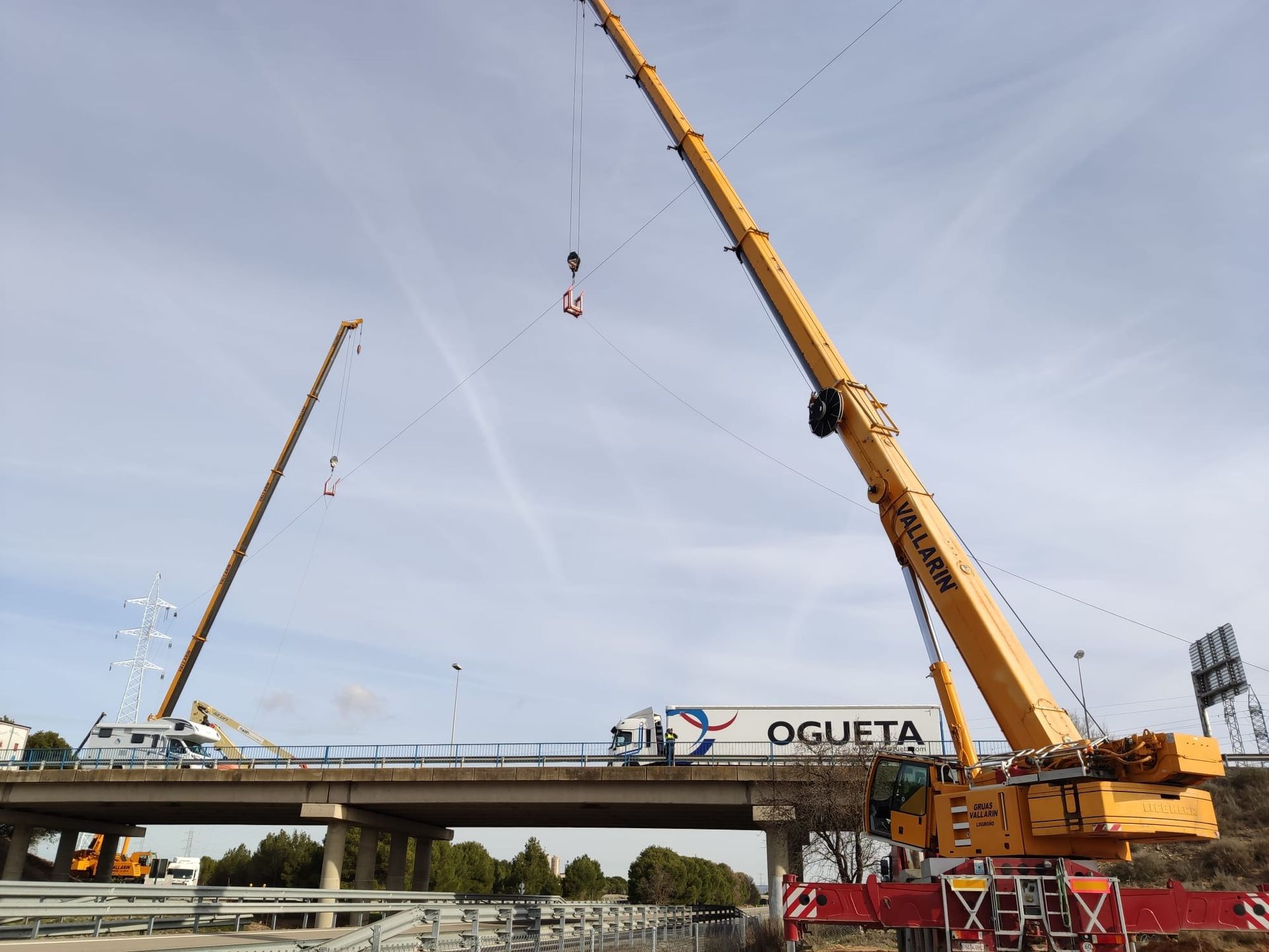 Una gran grúa amarilla está levantando un camión sobre un puente.