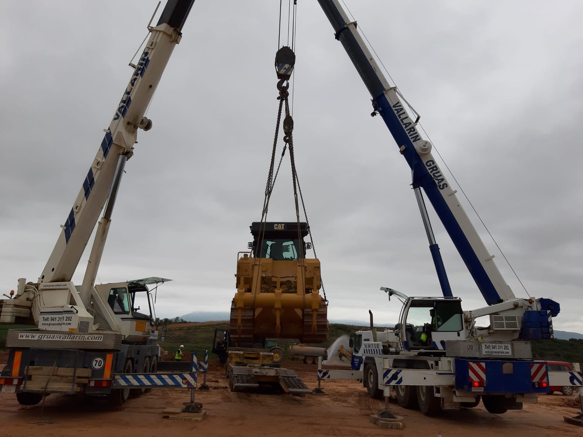 Una excavadora es levantada por dos grúas en un sitio de construcción.