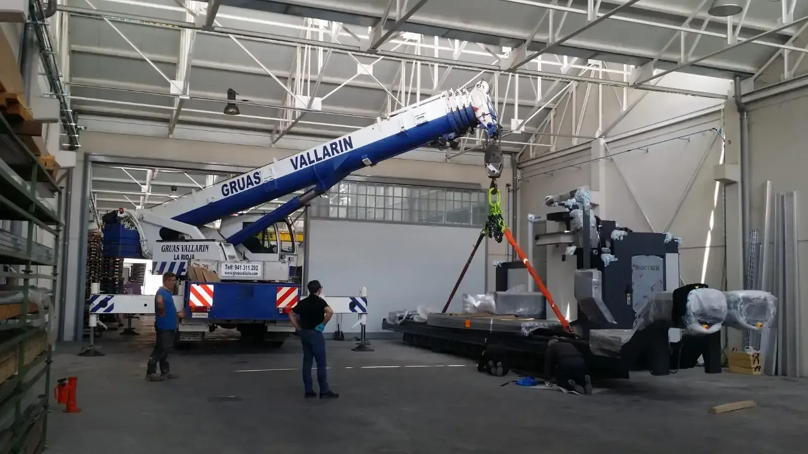 Un hombre está de pie junto a una grúa en un almacén.
