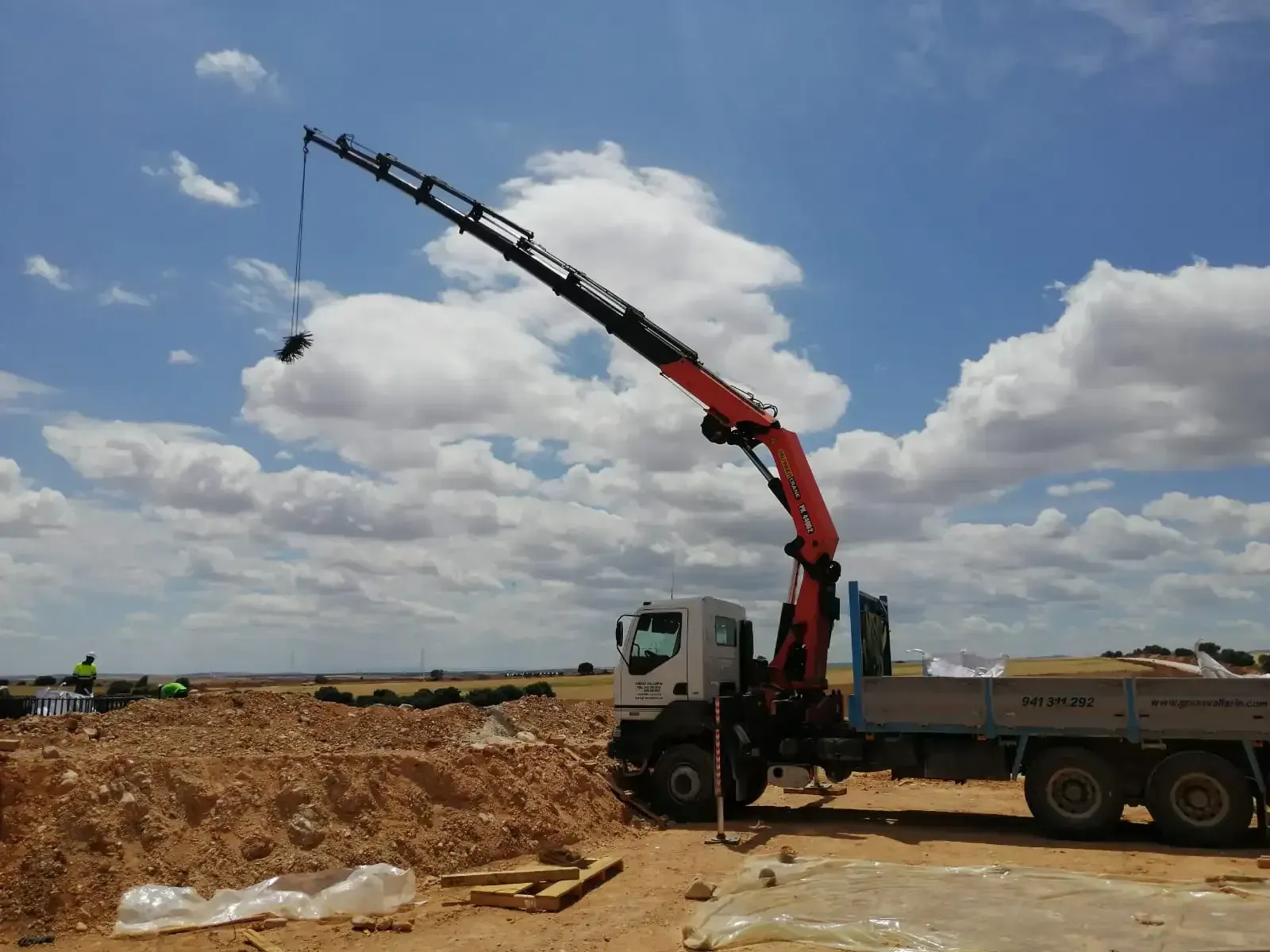 Un camión con una grúa acoplada está estacionado en un campo de tierra.