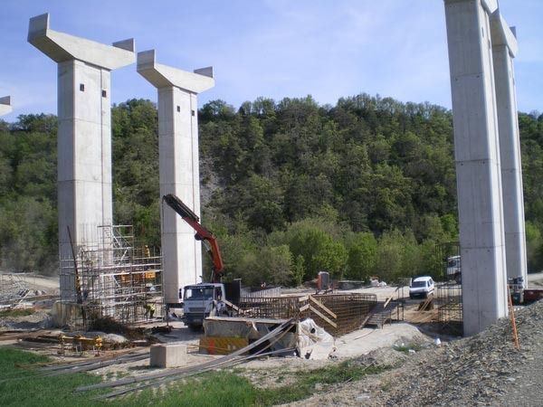 Un sitio de construcción con pilares de hormigón y árboles al fondo.