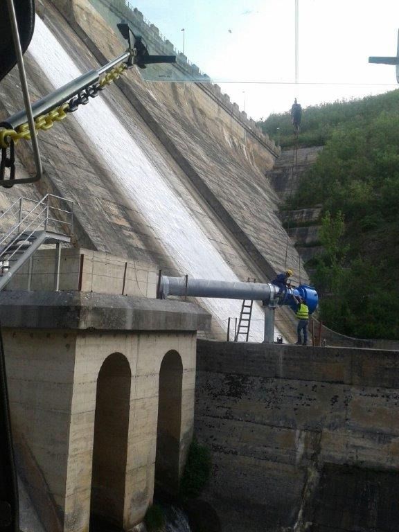 Un hombre con un chaleco amarillo está parado al costado de una presa.