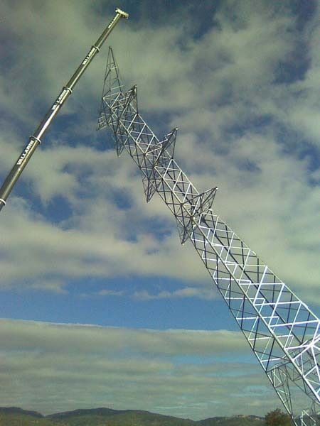 Una grúa está levantando una torre muy alta en el cielo.