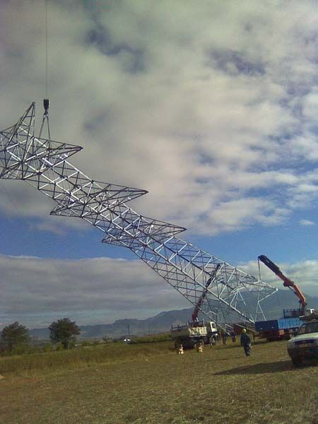 Una gran estructura metálica está siendo levantada por una grúa en un campo.