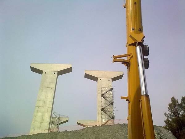 Una grúa amarilla está sentada encima de un montón de tierra junto a un puente en construcción.