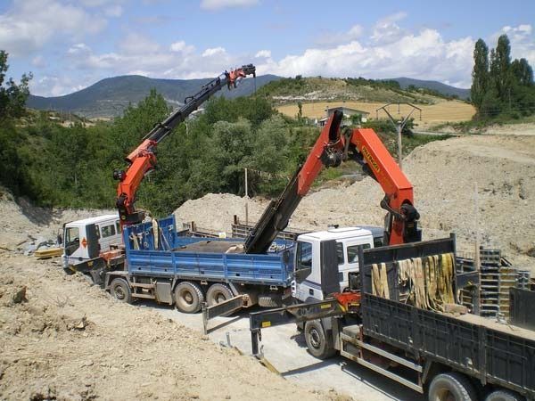 Una grúa está levantando un camión volquete en un campo de tierra.