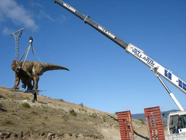 Una grúa está levantando una estatua de un dinosaurio.