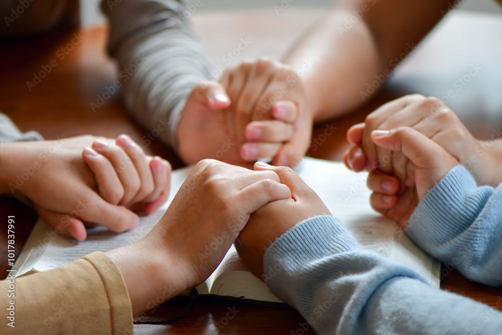 Die Hände sind zum Gebet um ein offenes Buch auf einem Holztisch gefaltet.