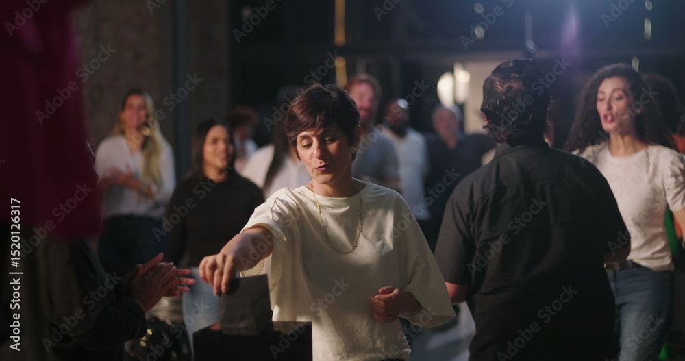 Menschen tanzen nachts im Freien, beleuchtet von Lichtern. Eine Frau in einem weissen Hemd gestikuliert.