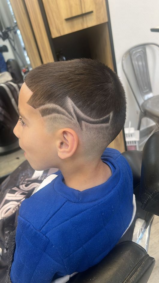 Garçon avec une coupe courte dégradée et des ondulations, assis dans un fauteuil de barbier dans un salon de coiffure.
