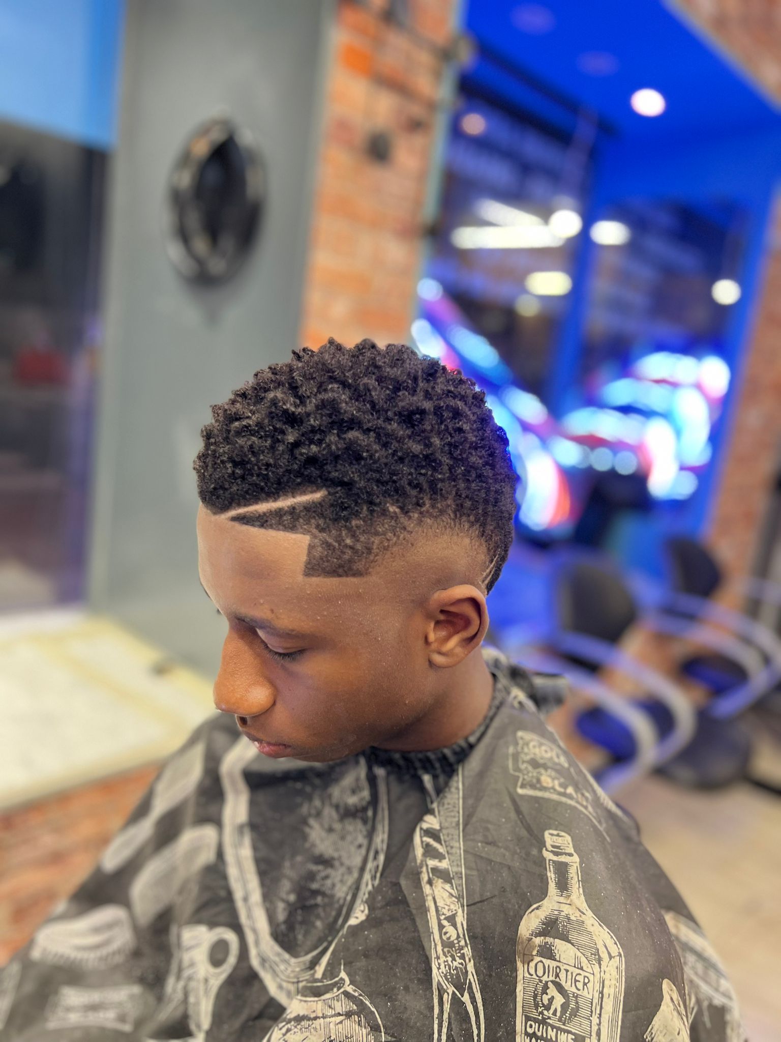 Profil latéral d'un homme avec une coupe dégradée fraîche dans un salon de coiffure, portant une cape de barbier.