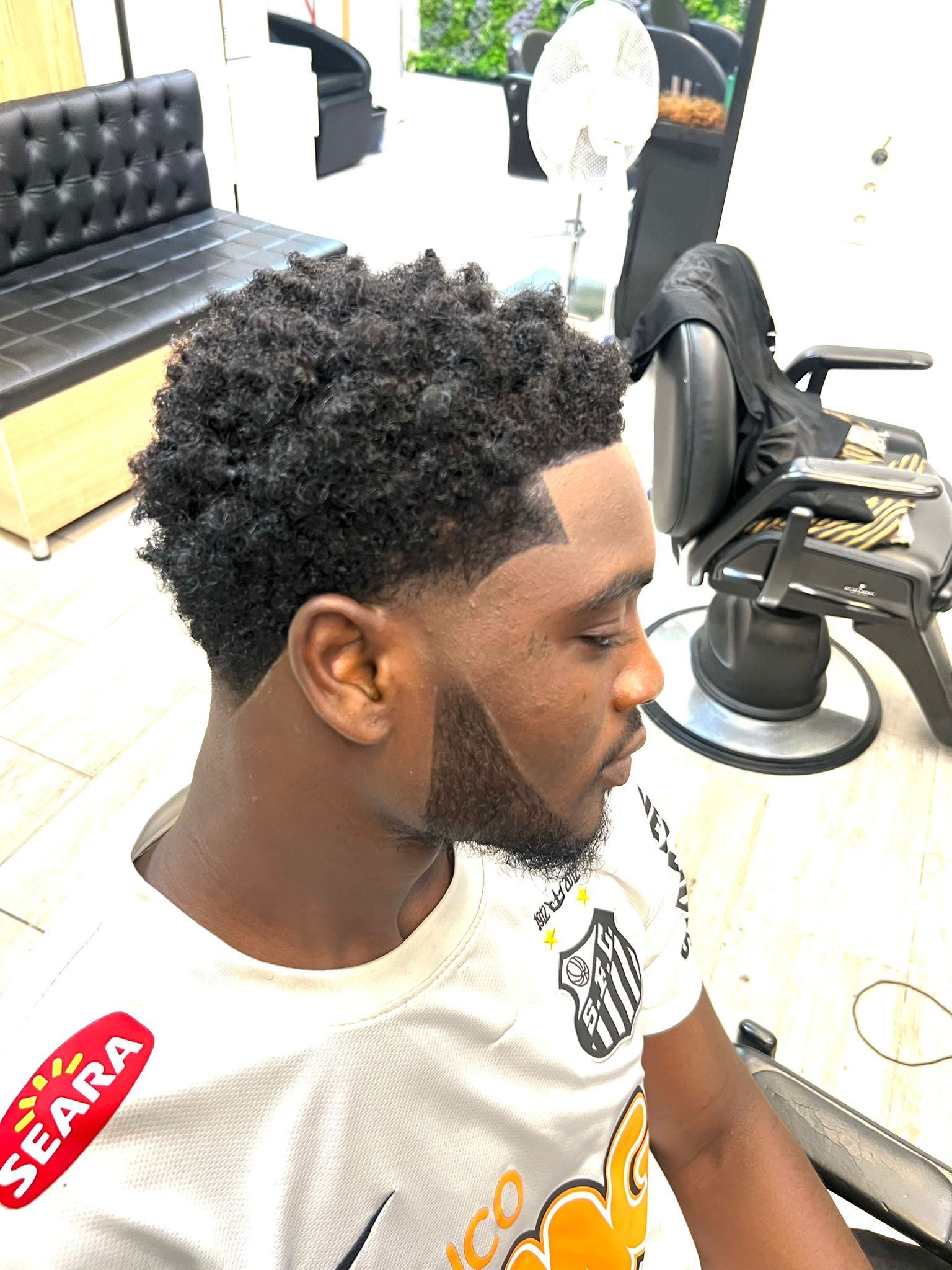 Portrait de profil d'un homme assis sur un fauteuil de barbier, arborant une coupe de cheveux bouclée dégradée.