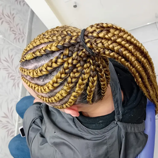 Vue de dessus de cheveux tressés blonds et noirs, rassemblés en chignon, avec une personne assise sur un fauteuil de salon