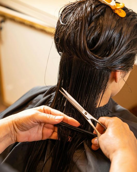 Coiffeuse coupant des cheveux foncés mouillés avec des ciseaux et un peigne dans un salon