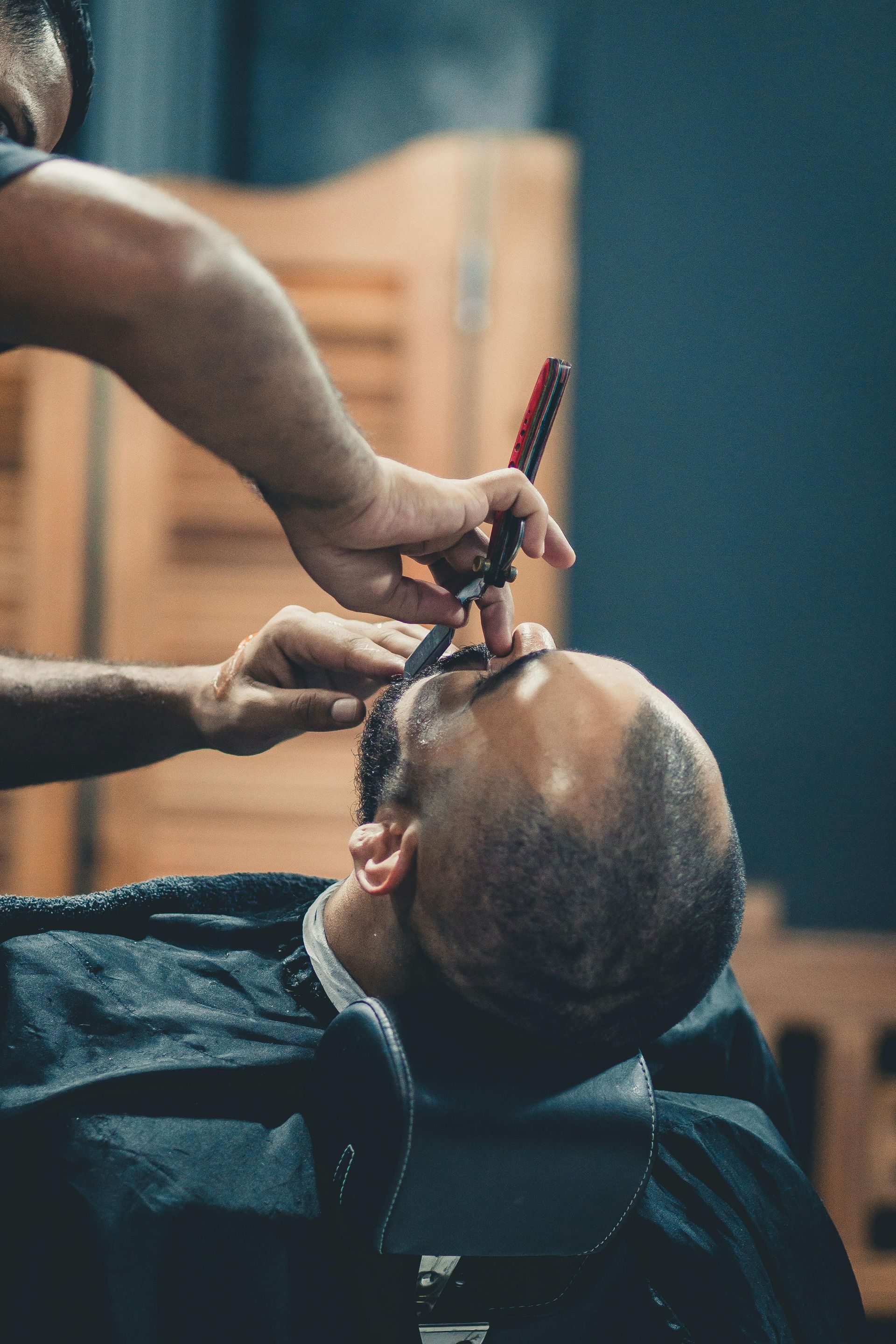Un coiffeur rase le visage d'un client avec un rasoir droit dans un salon de coiffure.