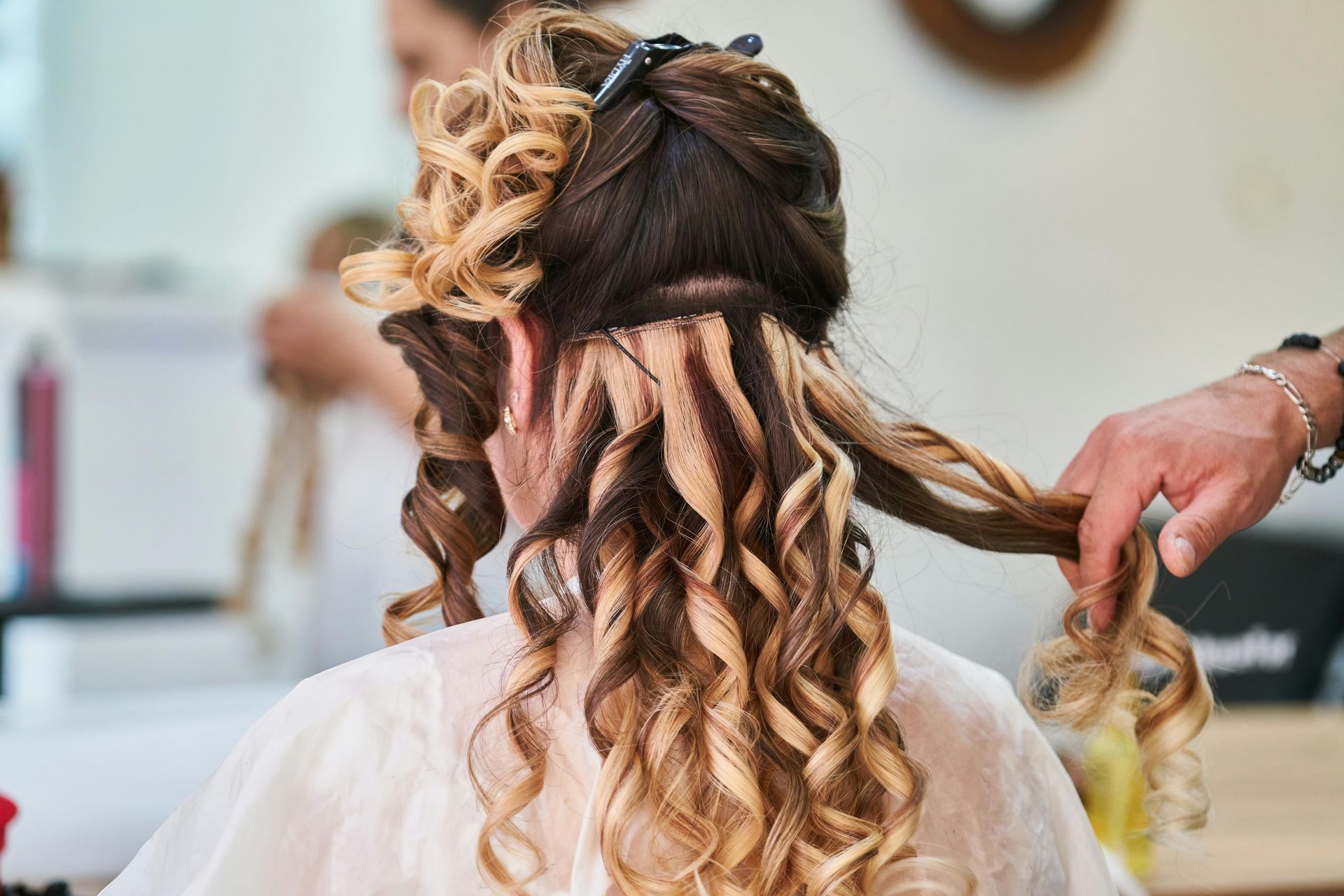 Une coiffeuse boucle de longs cheveux sur un fauteuil de salon, avec des ondulations blondes et brunes en cours de coiffage.
