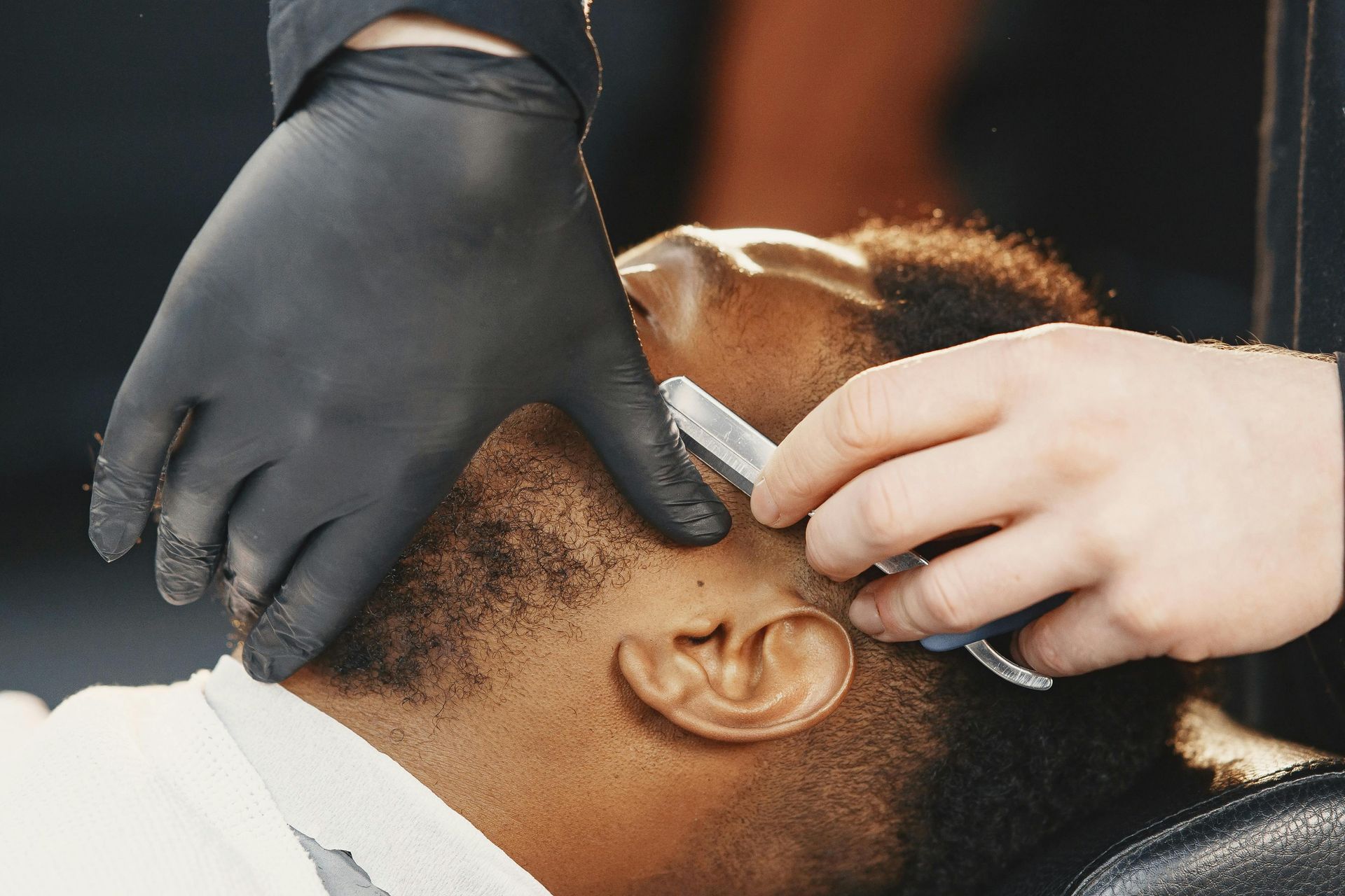 Des mains rasent la ligne des cheveux d'un client avec un rasoir droit dans un fauteuil de barbier