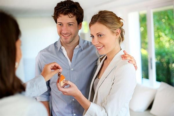 Agente inmobiliario entregando llaves a una pareja sonriente en una habitación luminosa y moderna.