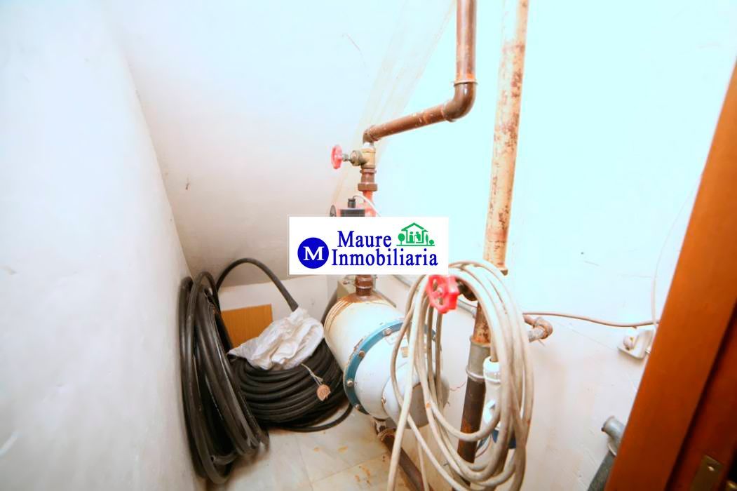 Fontanería y tuberías en una pequeña habitación blanca. Se ven un tanque de agua y mangueras enrolladas.