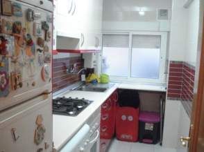 Cocina pequeña con gabinetes blancos, detalles en rojo y una ventana.