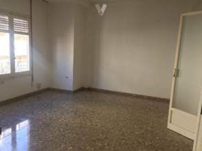 Habitación vacía con ventana, puerta y suelo moteado. Paredes blancas y luz natural.