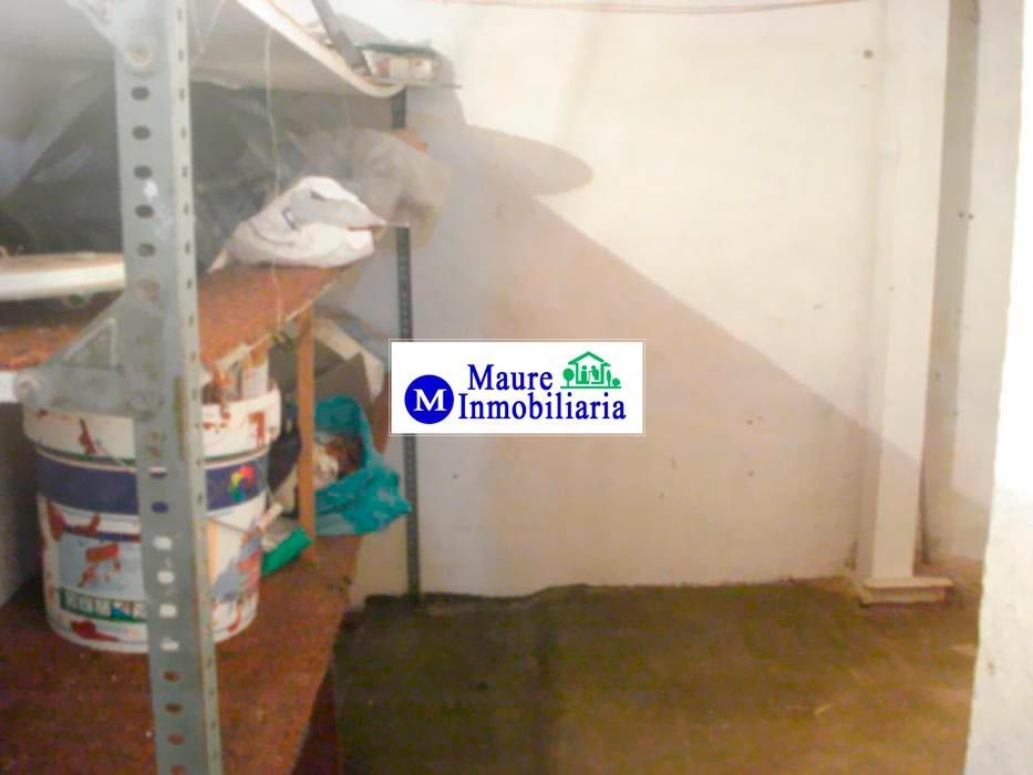 Área de almacenamiento con estanterías, botes de pintura y piso de concreto.