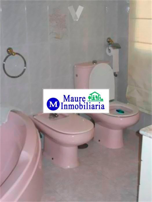 Sanitarios rosas: inodoro, bidé y bañera. Paredes de azulejos blancos. Logotipo de Maure Inmobiliaria.