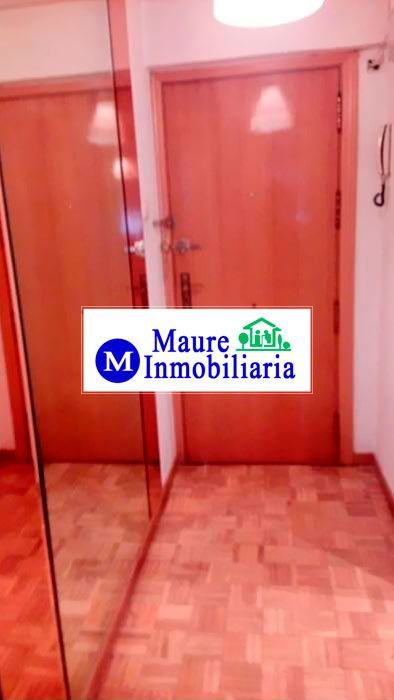 Pasillo con suelo y puertas de madera, una de ellas con espejo. Logotipo de Maurc Inmobiliaria visible.