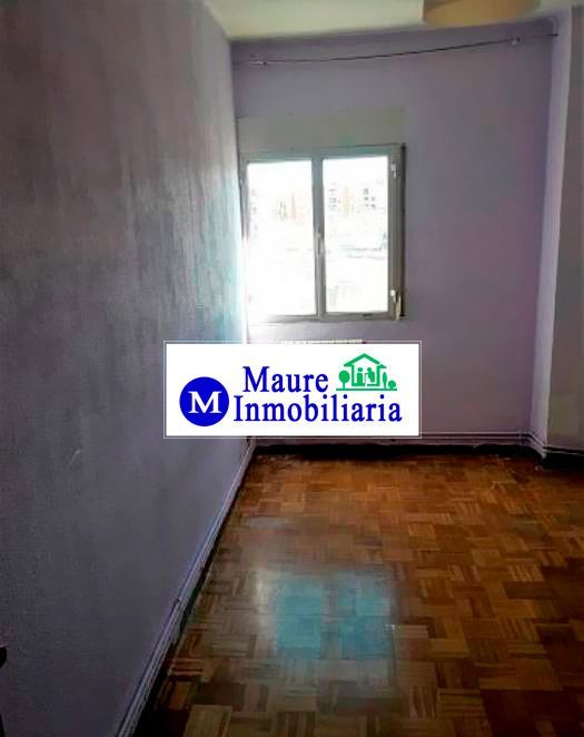 Habitación vacía con suelo de madera y ventana, probablemente un anuncio inmobiliario. Paredes moradas y logotipo de empresa.