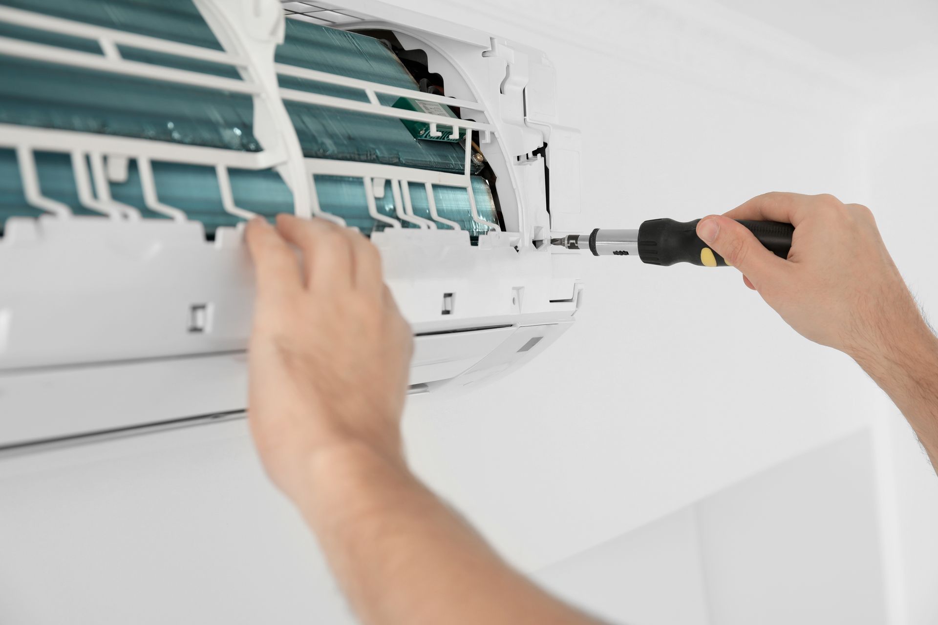 Des mains utilisant un tournevis pour réparer un climatiseur mural dont le capot est ouvert