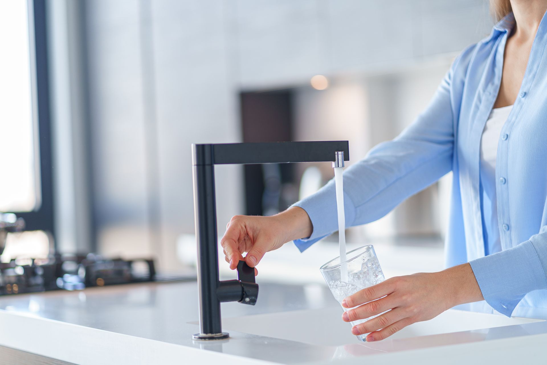 Personne remplissant un verre d’eau au robinet de la cuisine