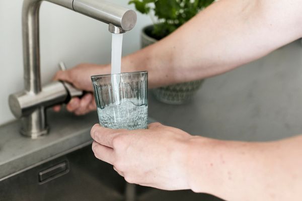 Des mains remplissant un verre d’eau au robinet de la cuisine