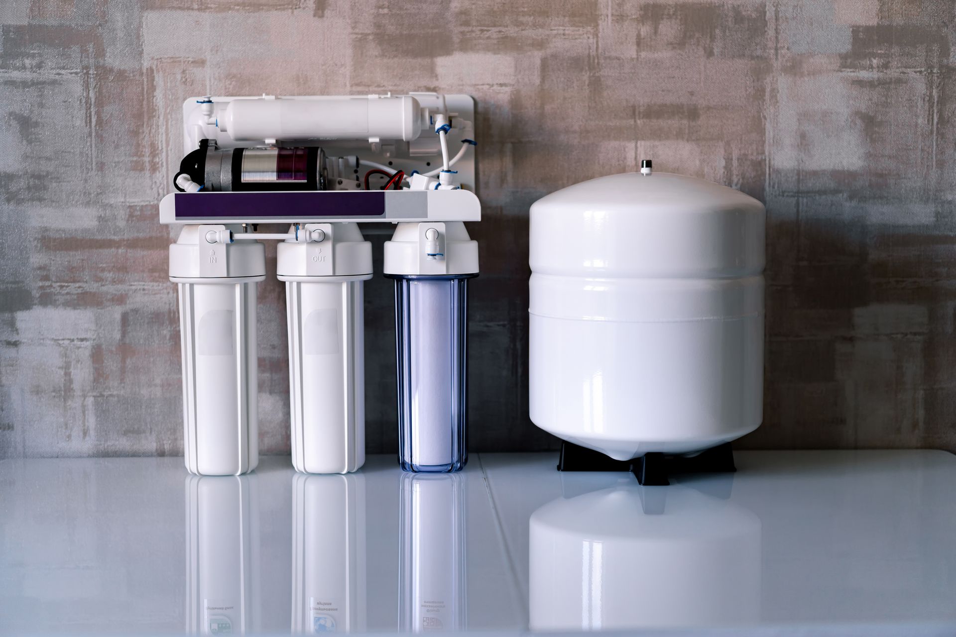 Système de purification de l’eau avec des cartouches filtrantes blanches et un réservoir de stockage.