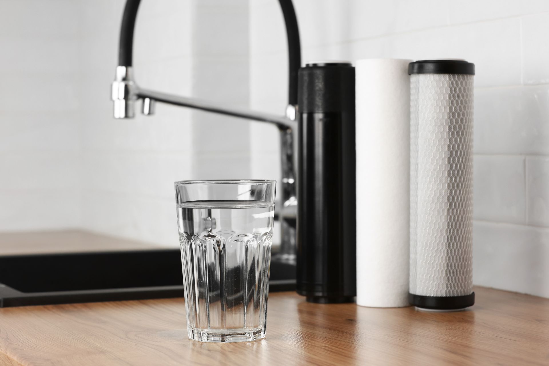 Plan de travail de cuisine avec un robinet, un verre d’eau et deux cartouches de filtre à eau