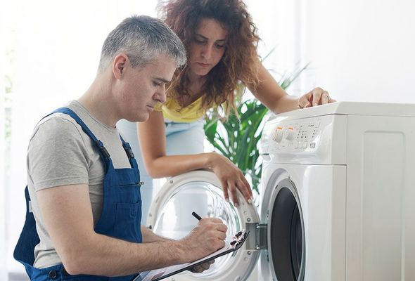 Ein Mann repariert eine Waschmaschine, während eine Frau zusieht.