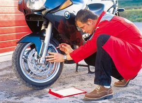 Mann kniet vor Motorrad und prüft Vorderrad