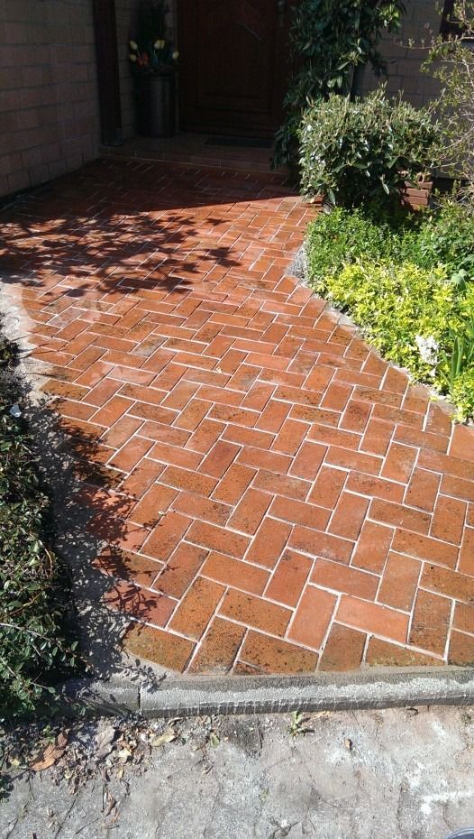 Ein mit Ziegelsteinen im Fischgrätmuster gepflasterter Weg führt zur Eingangstür, die von Grünpflanzen und einer steinernen Garteneinfassung gesäumt ist.