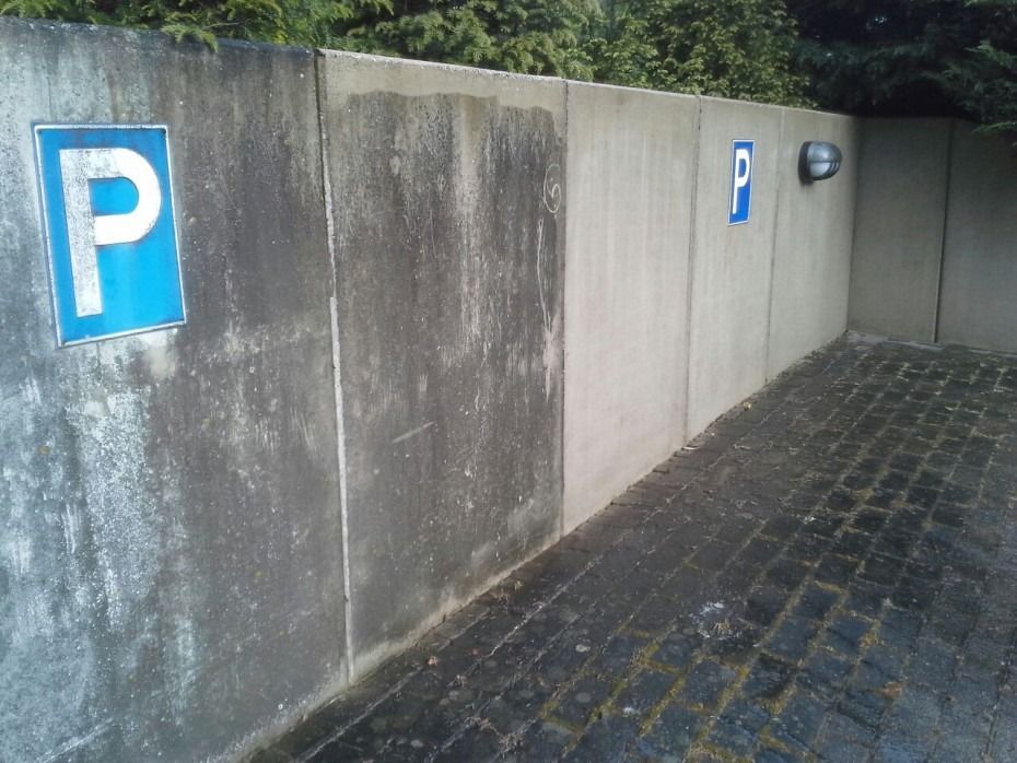 Zwei blaue Parkschilder an einer hohen, gegliederten Betonmauer neben einer gepflasterten Auffahrt.