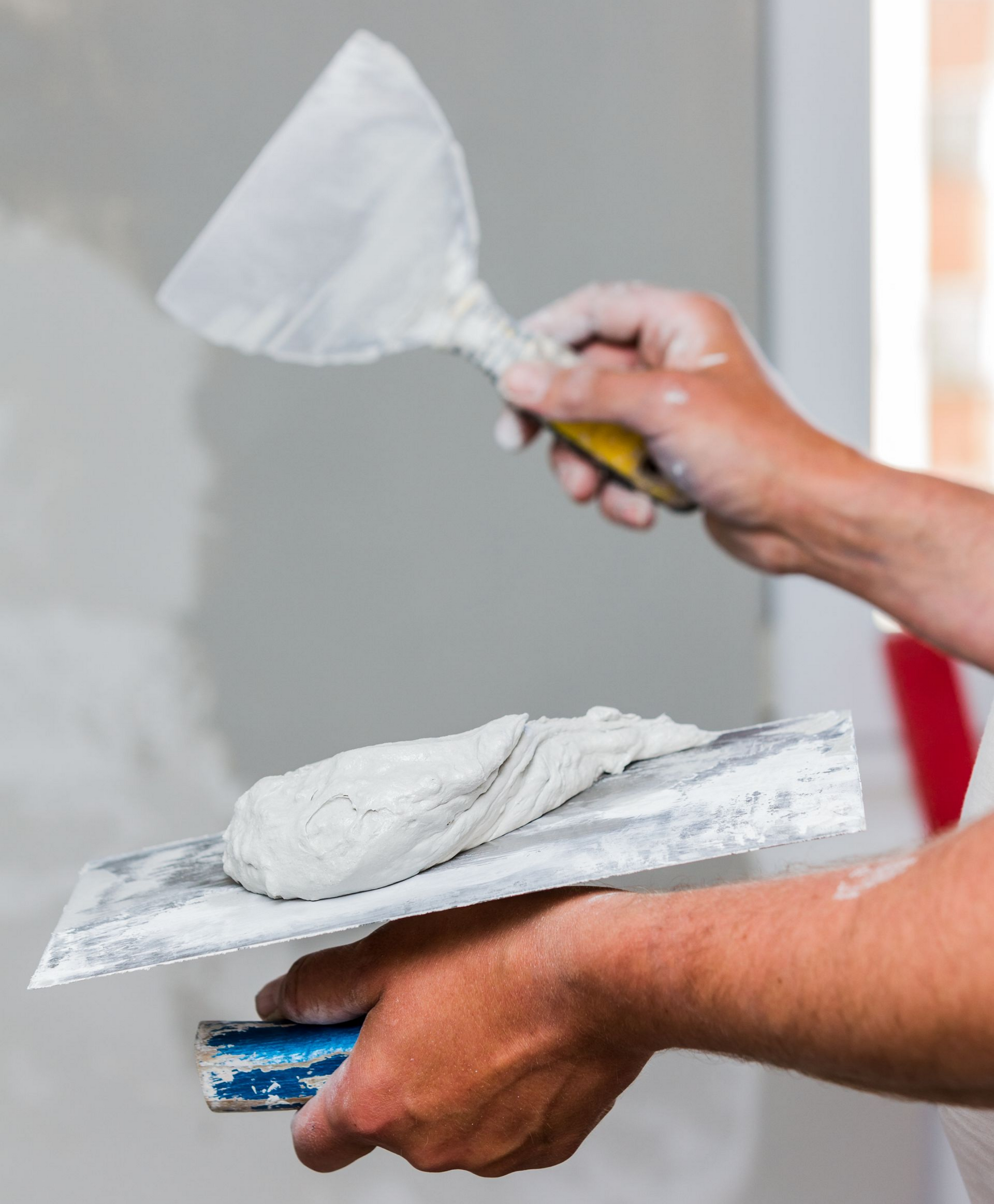 Personne appliquant du plâtre sur un mur à l'aide d'une truelle.
