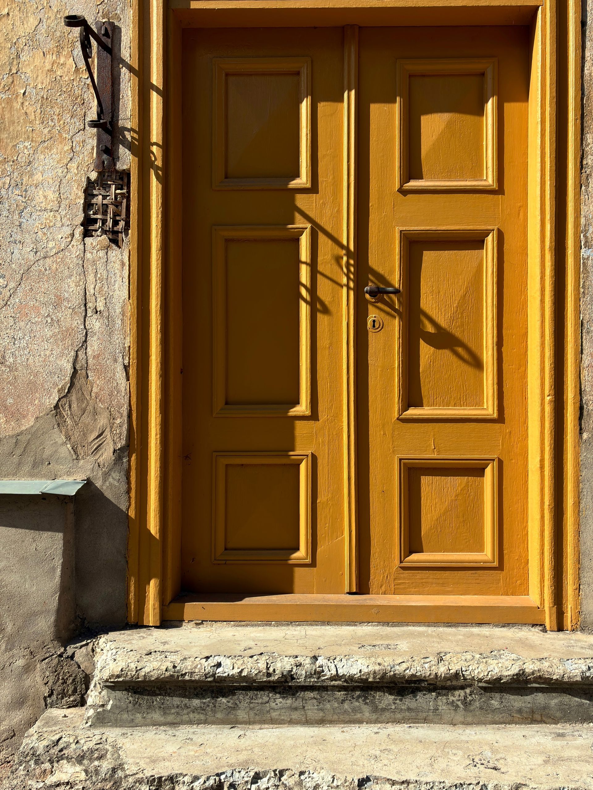 Double porte jaune à panneaux décoratifs sur un bâtiment en pierre patinée.