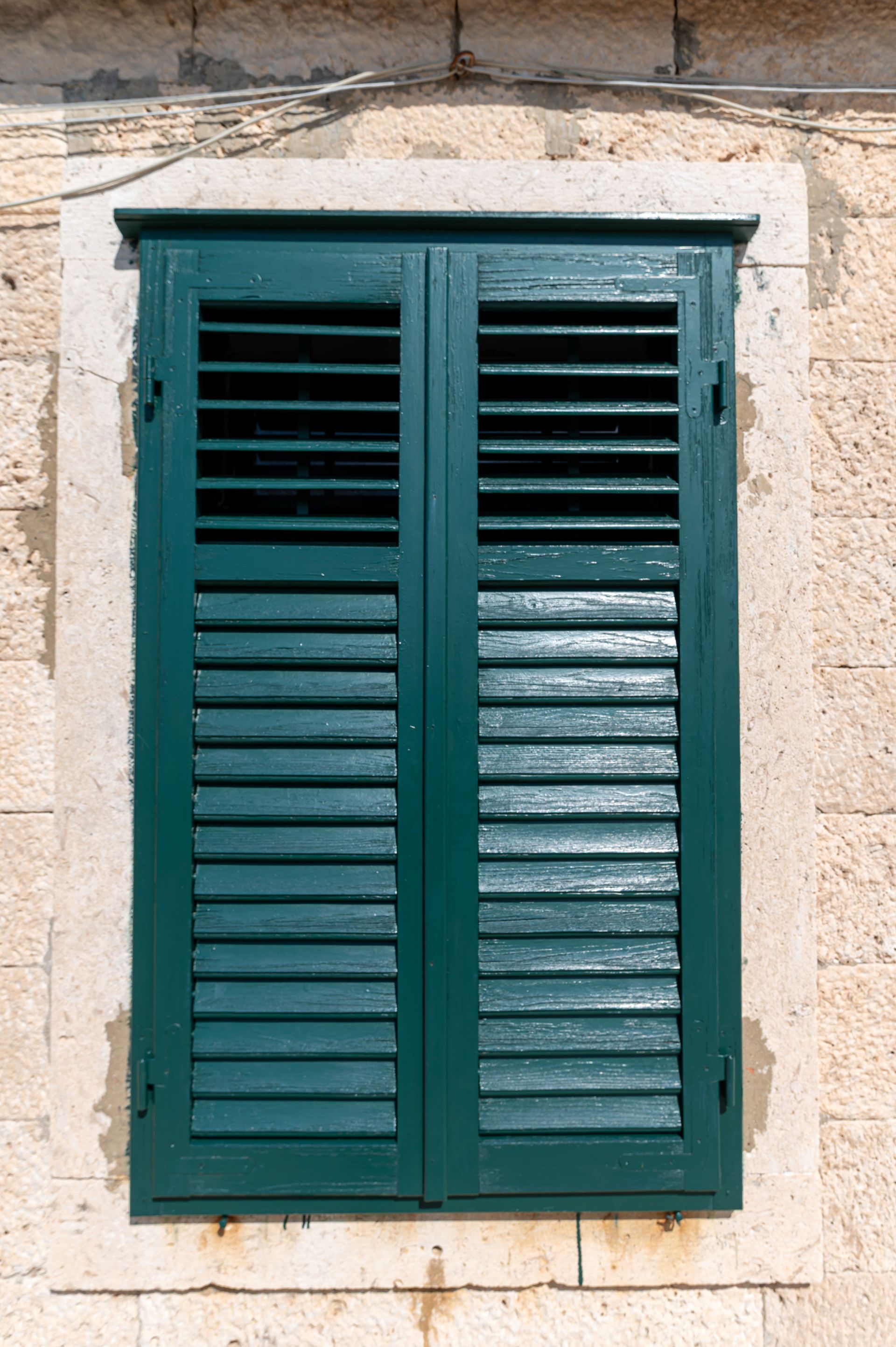 Fenêtre à volets verts sur un bâtiment en pierre.