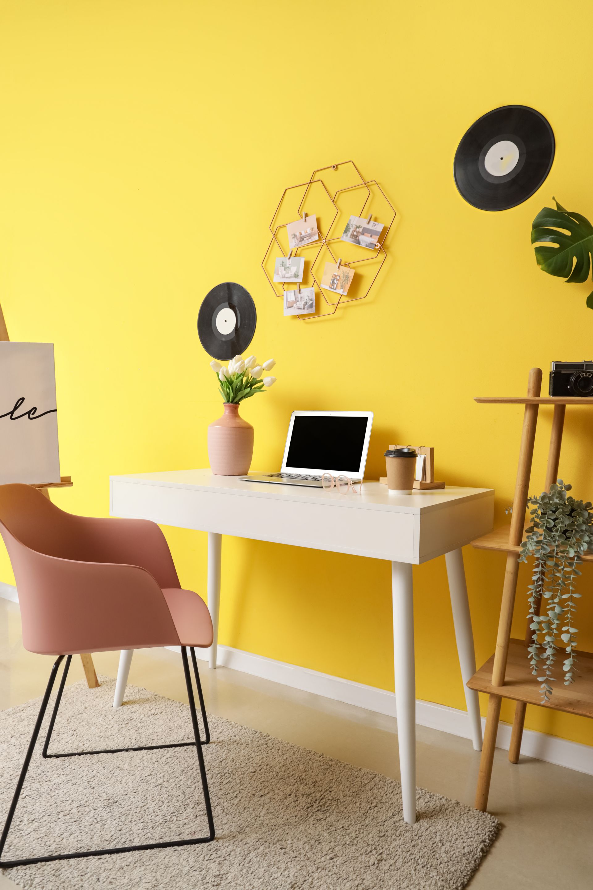 Un bureau contre un mur jaune, avec une chaise rose et des disques vinyle décoratifs sur le mur.