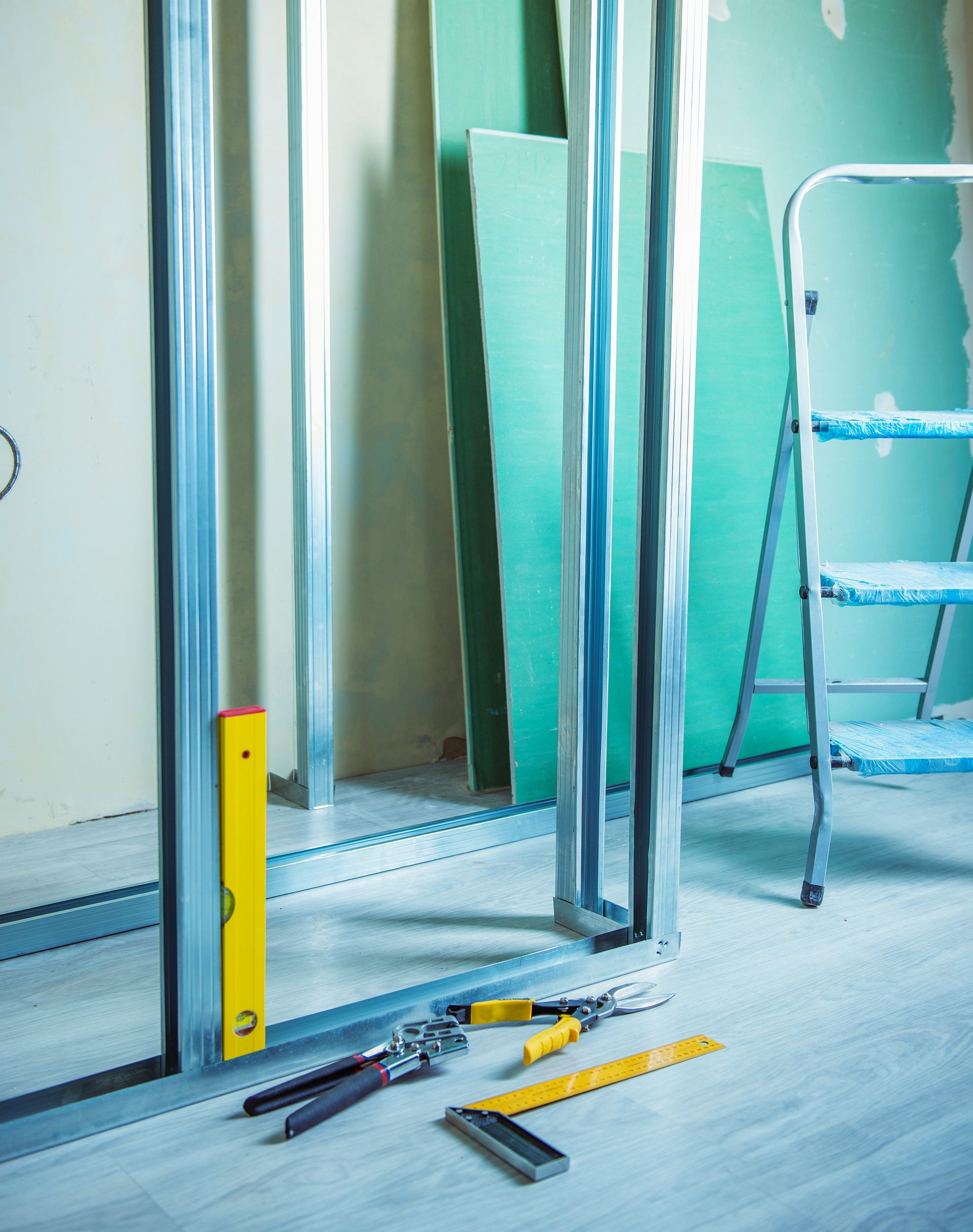 Chantier de construction avec ossature métallique, cloisons sèches, outils et échelle.