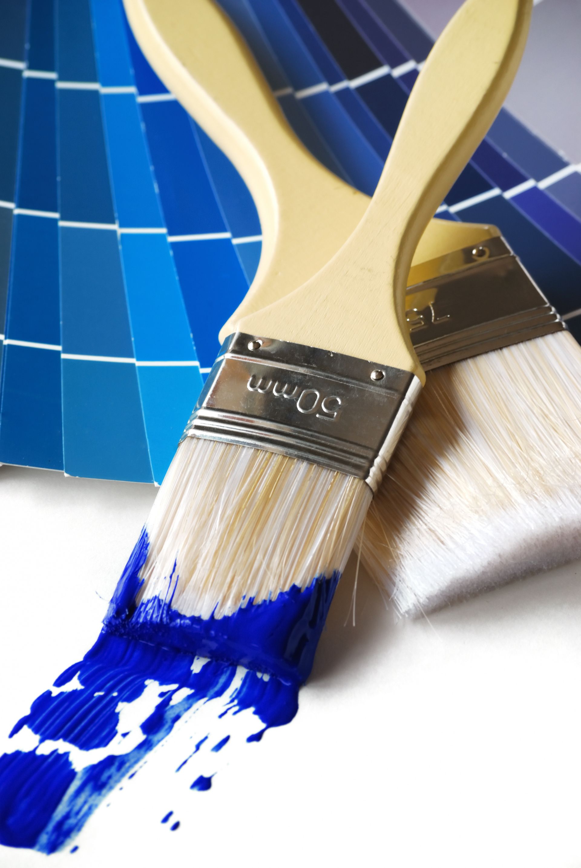 Deux pinceaux chargés de peinture bleue, appuyés contre un échantillon de peinture bleue.