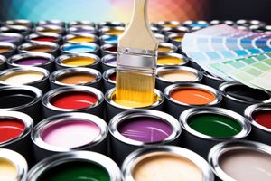 Des pots de peinture de différentes couleurs, un pinceau trempé dans de la peinture jaune et un échantillon de couleur.