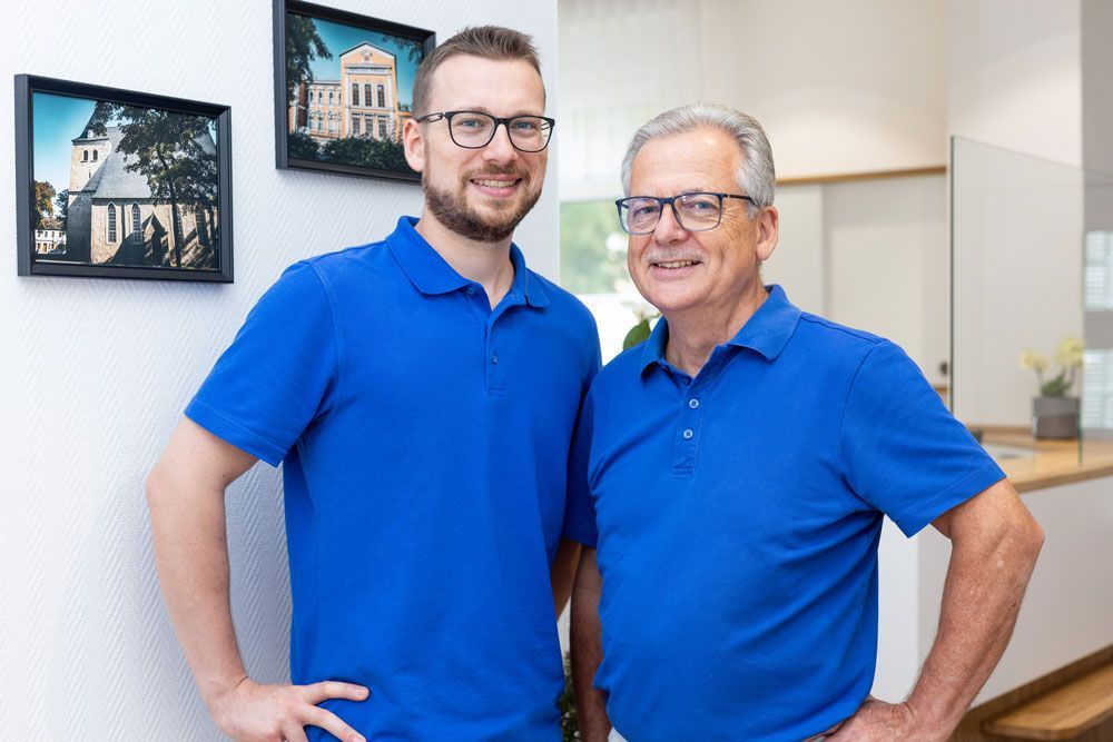 Zwei Männer in blauen Hemden stehen lächelnd in einem Büro.
