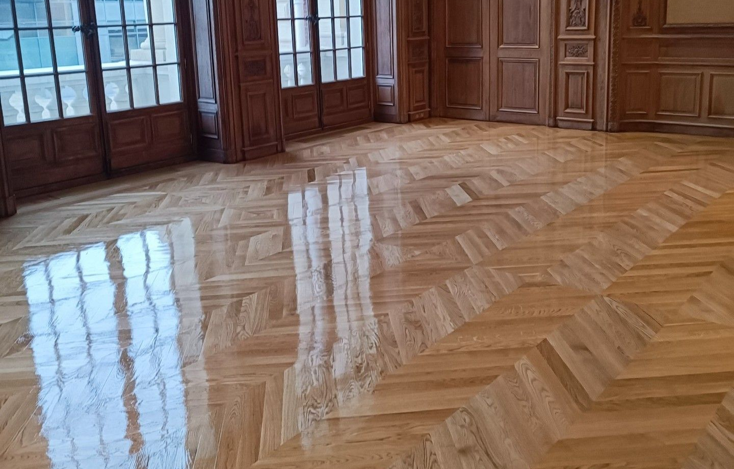 Dans une pièce lambrissée, le parquet clair reflète la lumière d'une fenêtre.