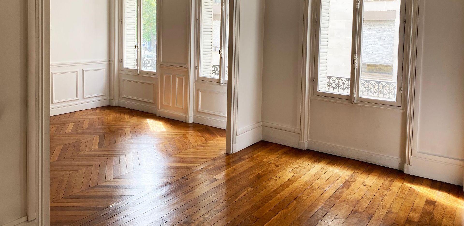 Sol en bois dans une pièce vide aux murs et fenêtres blancs.