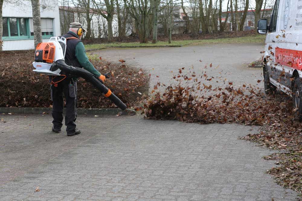 Ein Mann bläst auf einem Parkplatz Blätter vom Boden.